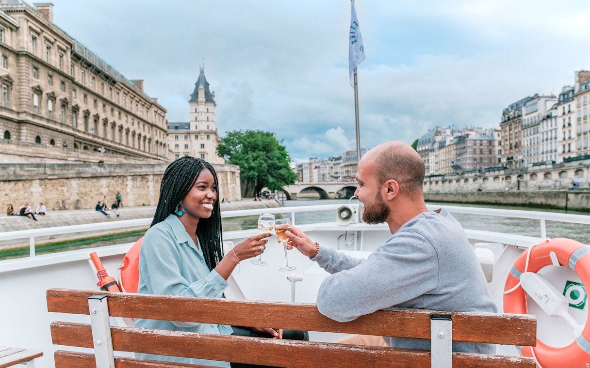Couple enjoying a Seine River cruise in Paris with historic buildings in the background.