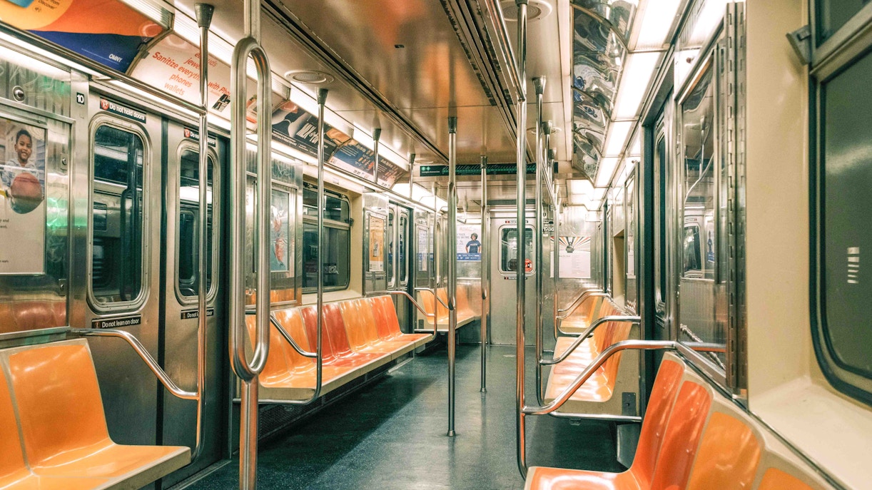 Empty New York City subway car with orange seats and metal poles.