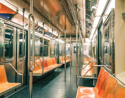 Empty New York City subway car with orange seats and metal poles.
