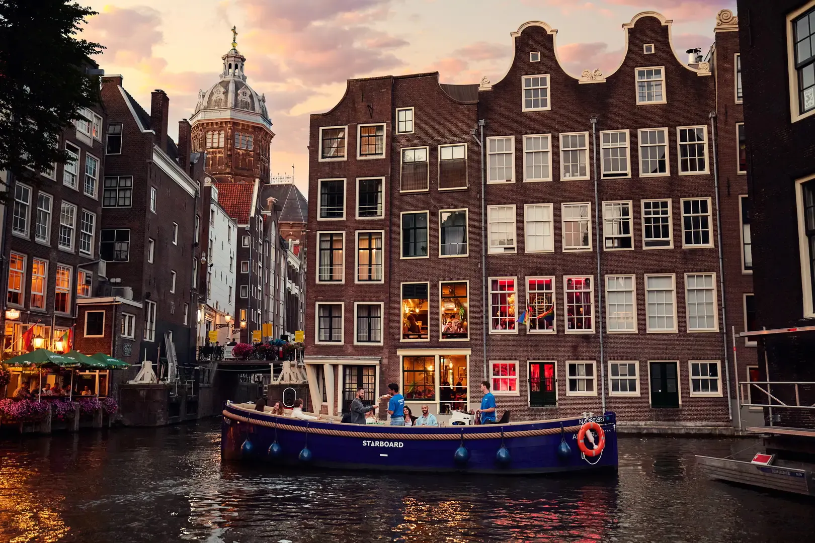 Open boat cruise on Amsterdam canal with historic buildings at sunrise.