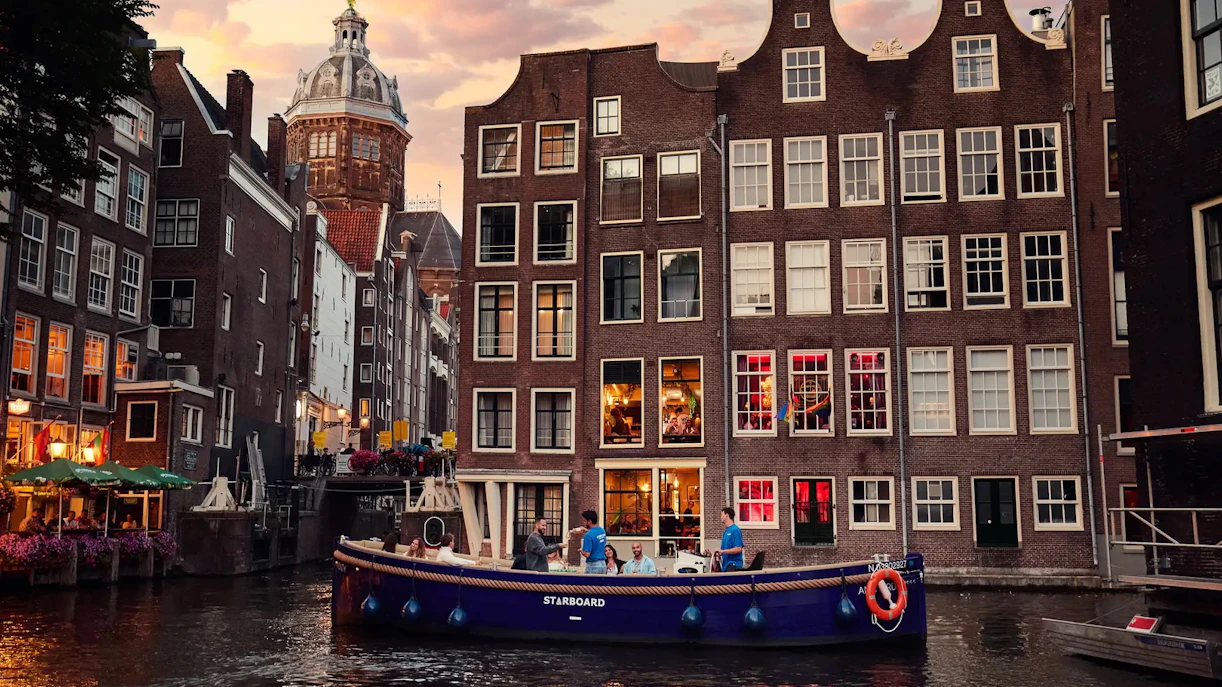 Open boat cruise on Amsterdam canal with historic buildings at sunrise.