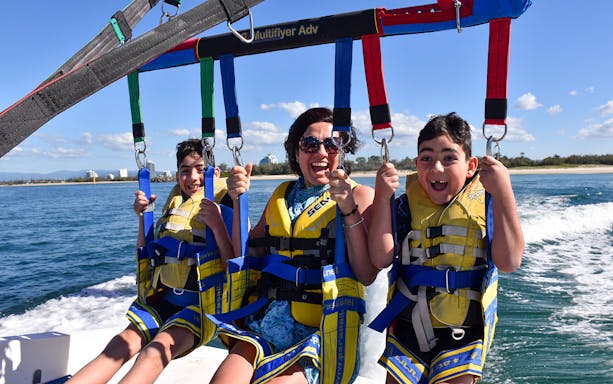 Group enjoying parasailing over water with city skyline in the background.