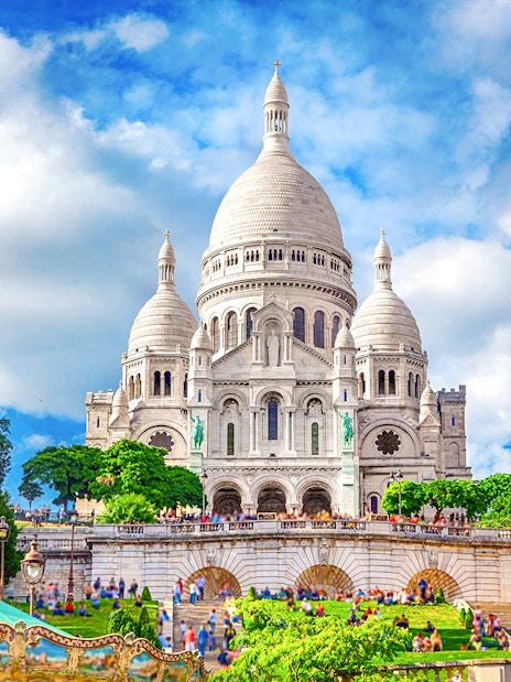 Sacre-Coeur Basilica in Montmartre, Paris, with tourists and greenery.