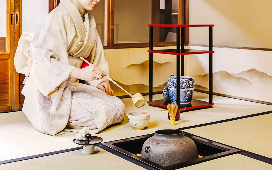 Person performing traditional Japanese tea ceremony with matcha tools.