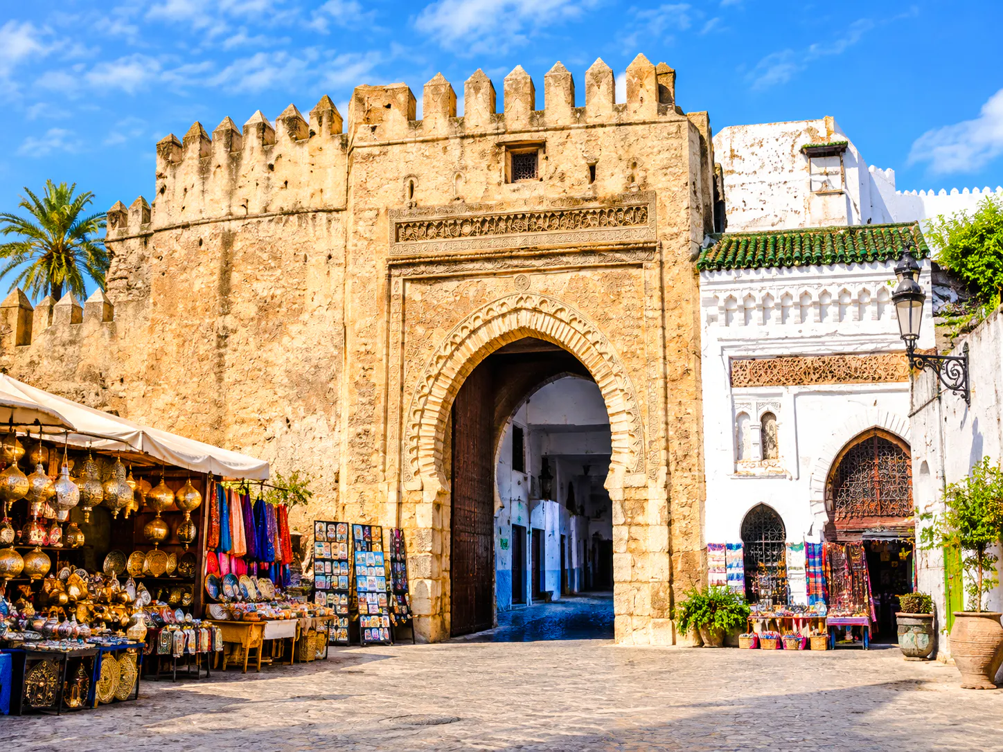 Kasbah gate with market stalls displaying lanterns and textiles, Tangier.