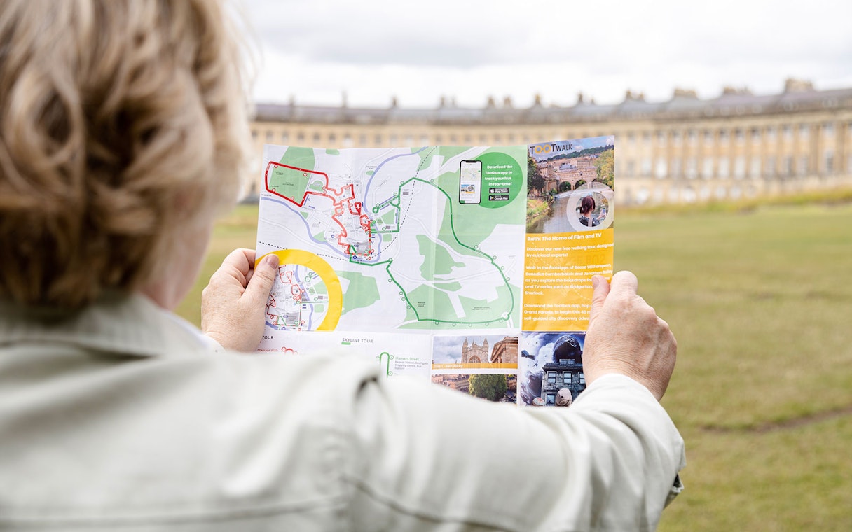 Tourist holding a Toot bus route map in front of the Royal Crescent, Bath.