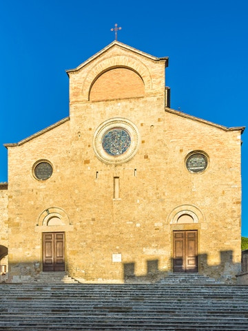 San Gimignano Cathedral facade with stone steps under clear blue sky.