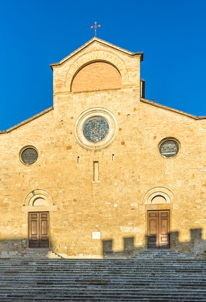 San Gimignano Cathedral facade with stone steps under clear blue sky.