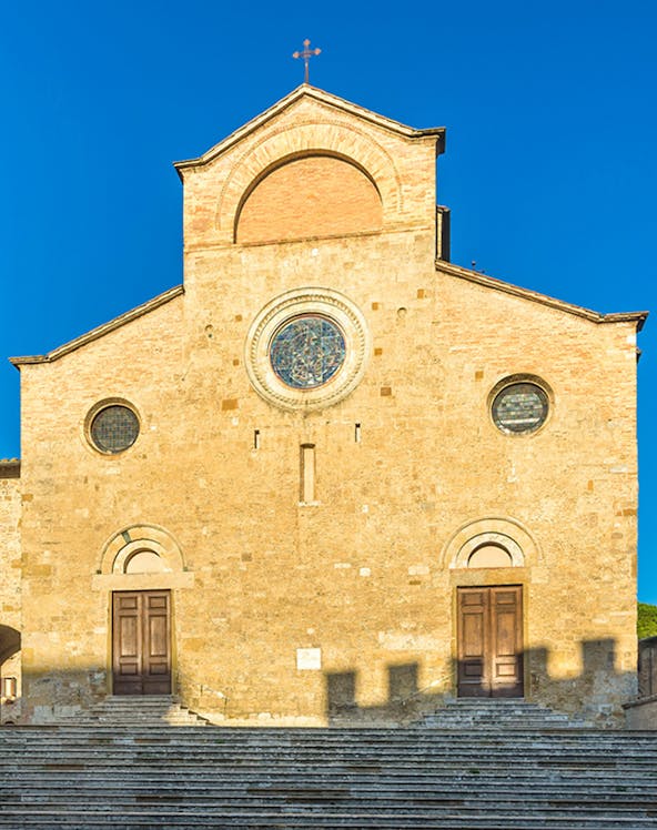 San Gimignano Cathedral facade with stone steps under clear blue sky.