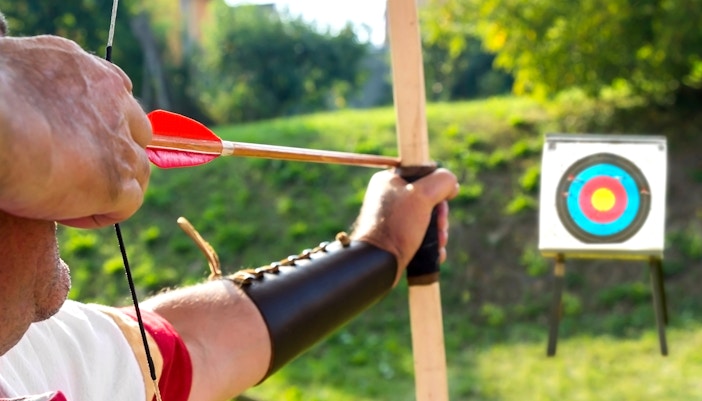 Archer aiming at a target during an archery experience in a green outdoor setting.