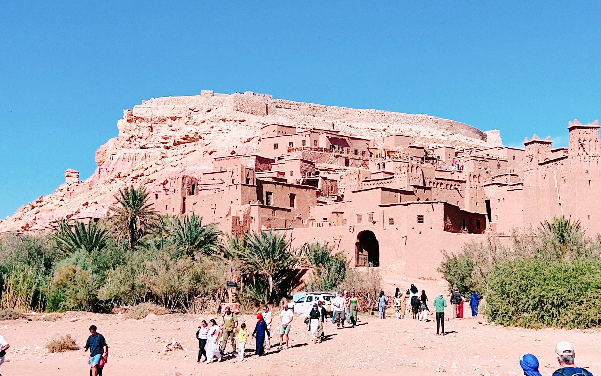 Ait Benhaddou kasbah with tourists walking, part of 3 Days Desert Tour to Merzouga Dunes.
