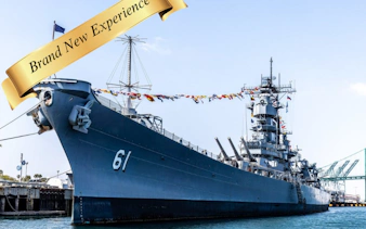 Battleship with flags docked at harbor for self-guided experience.