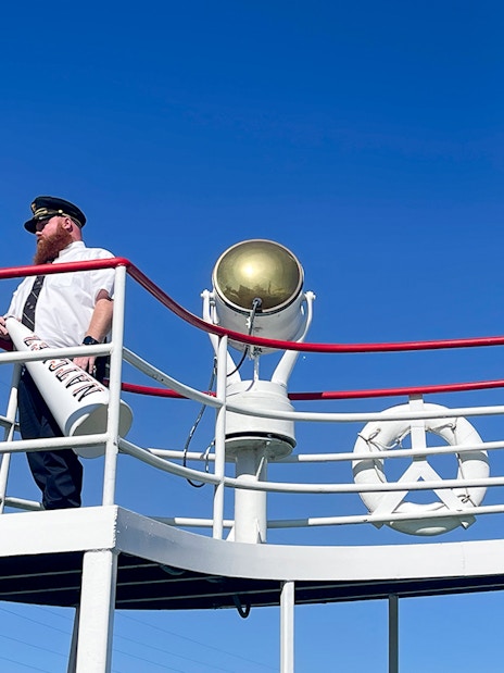 Captain on deck of the Steamboat Natchez with megaphone and flag.