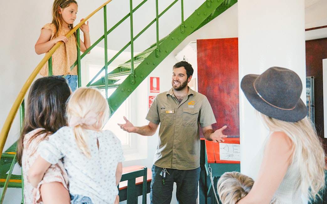 Tour guide explains to family inside Cape Naturaliste Lighthouse near spiral staircase.