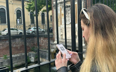 Person using a smartphone for a self-guided city exploration game near a canal in Milan Navigli.