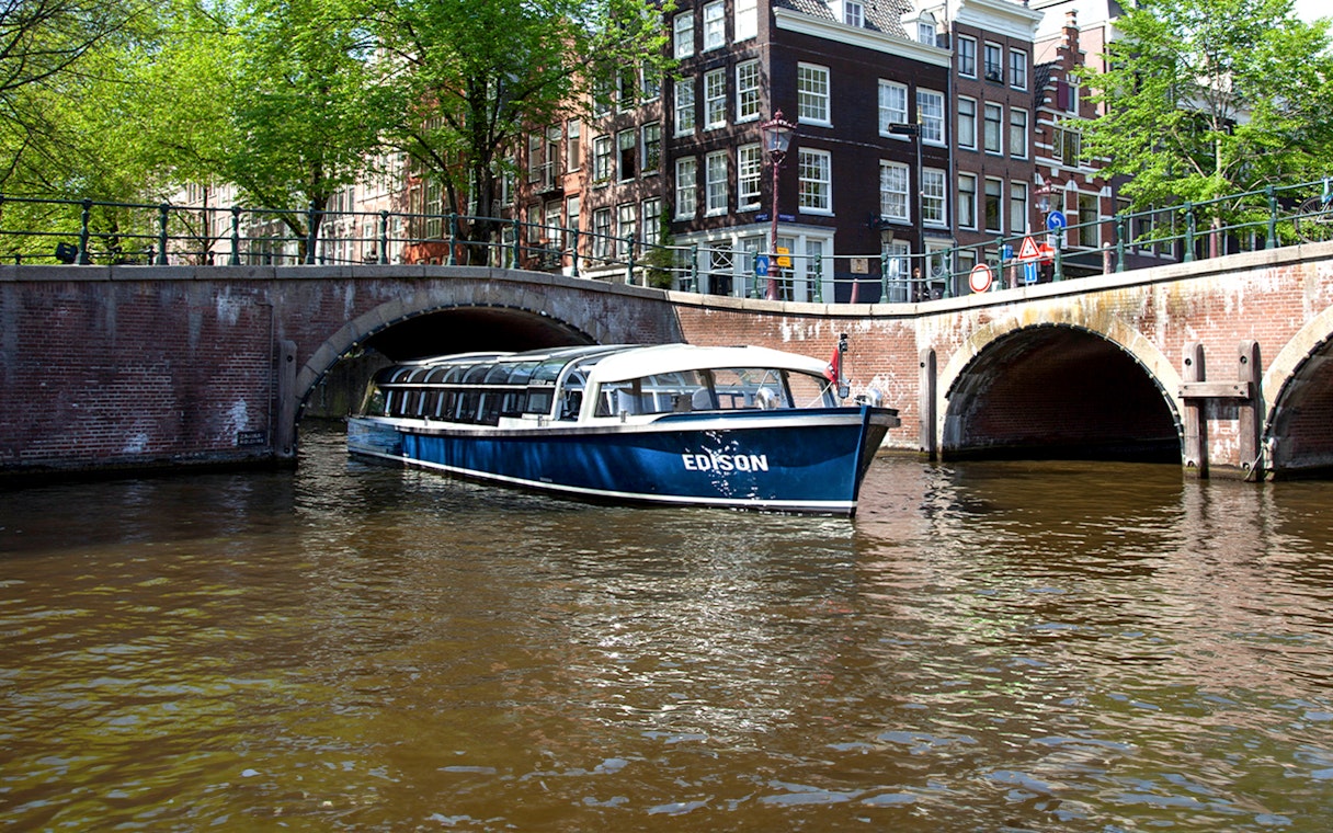 Canal cruise boat passing under a bridge in Amsterdam.