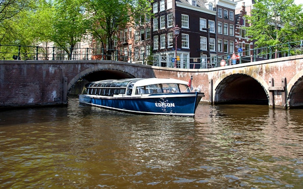 Canal cruise boat passing under a bridge in Amsterdam.