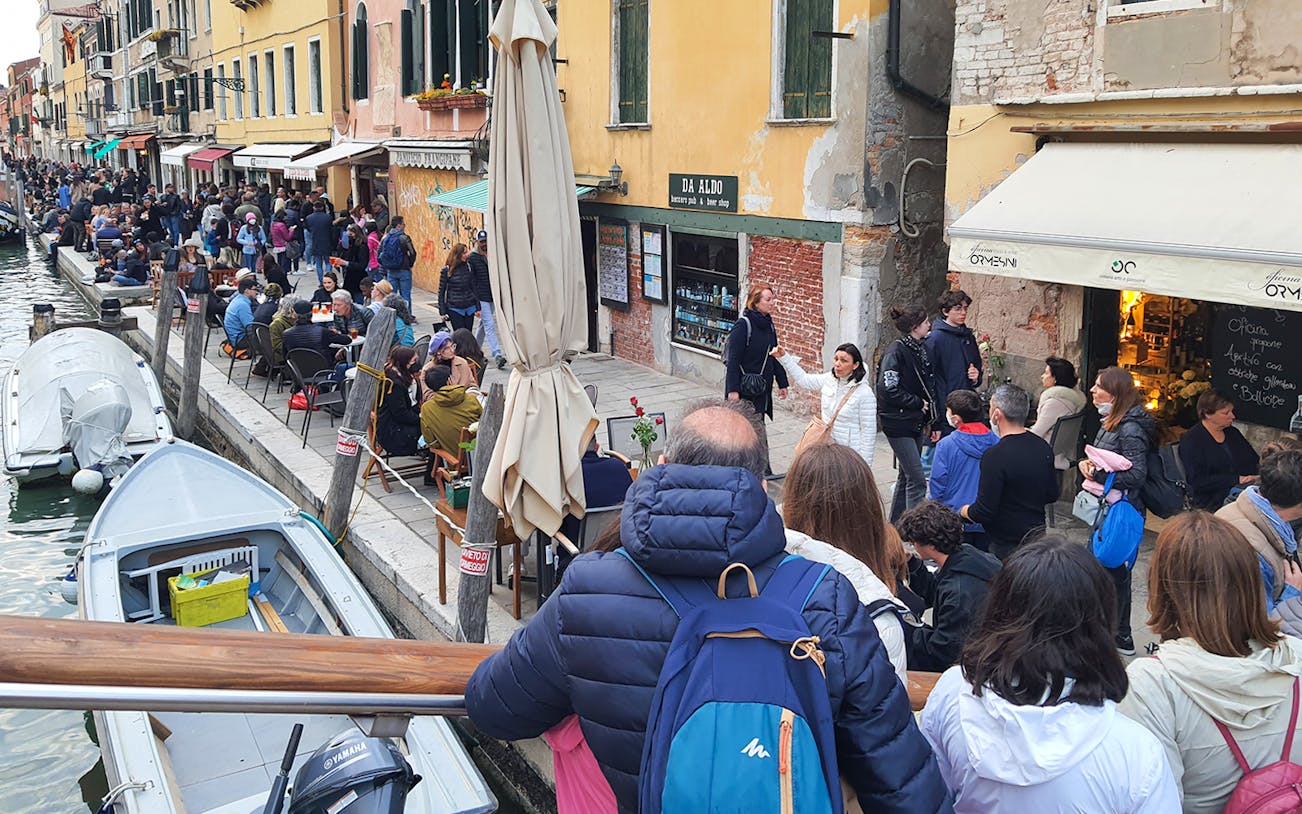 Venice canal-side dining and sightseeing tour with people enjoying street food.