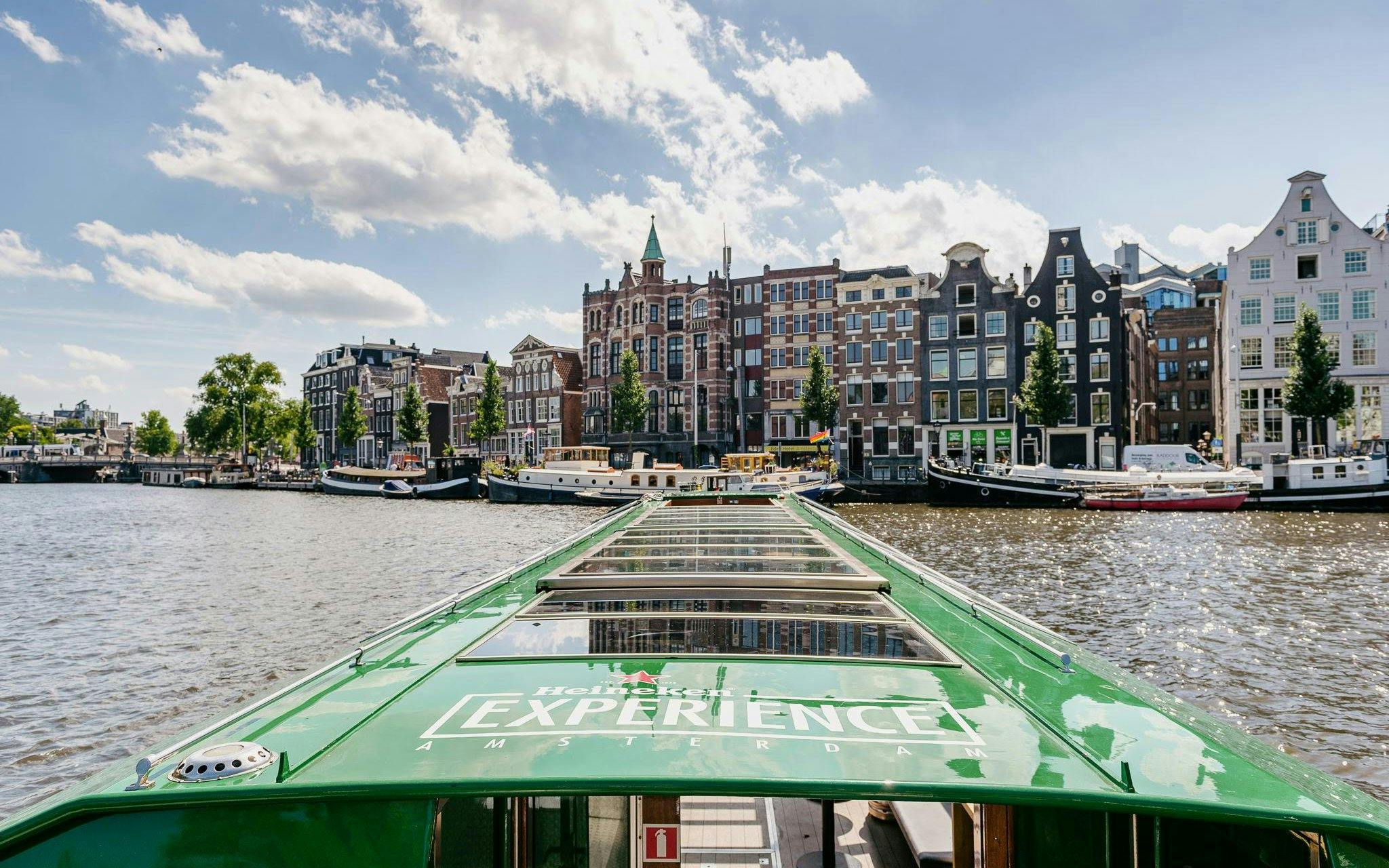 Heineken cruise boat on Amsterdam canal with historic buildings in the background.