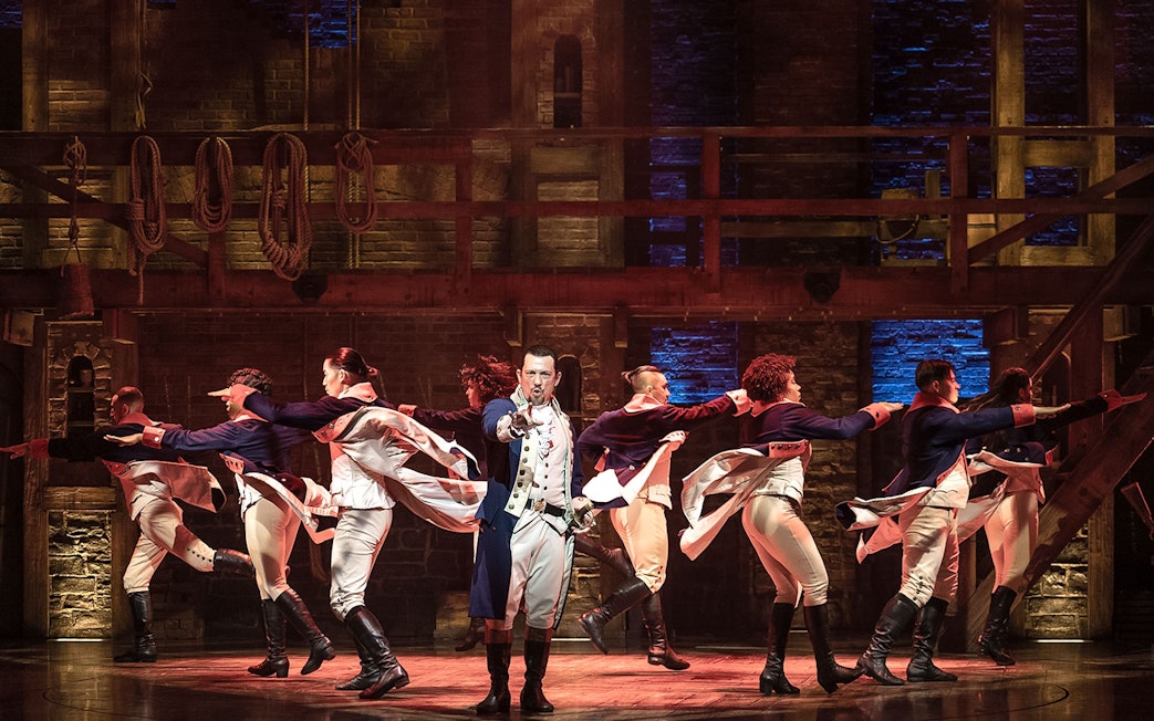 Cast performing a dance number in the musical Hamilton on stage.