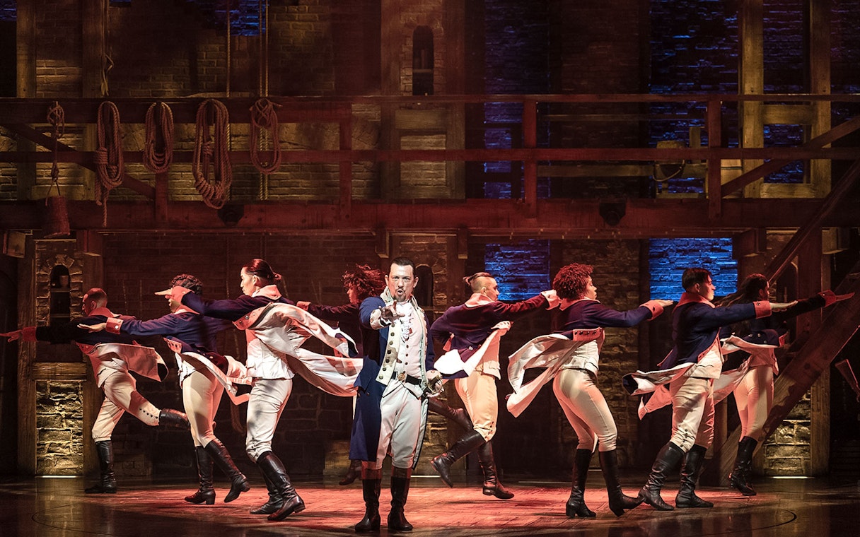 Cast performing a dance number in the musical Hamilton on stage.