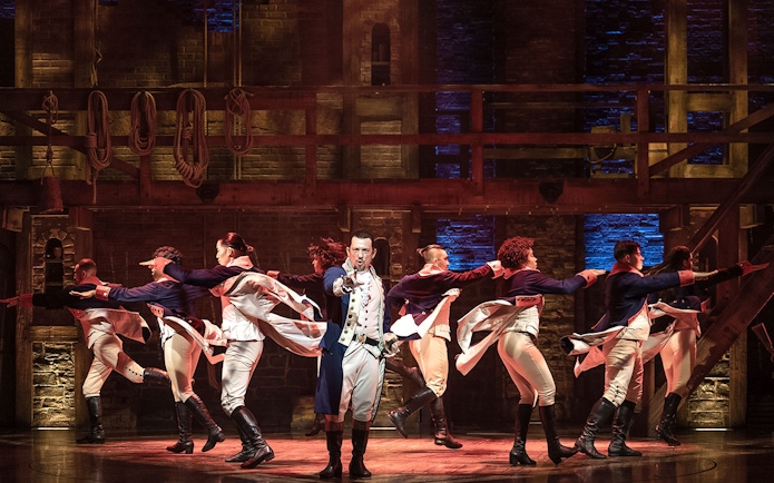 Cast performing a dance number in the musical Hamilton on stage.