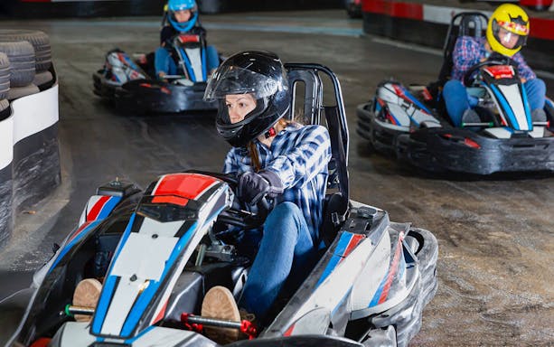 People racing go-karts on an indoor track.