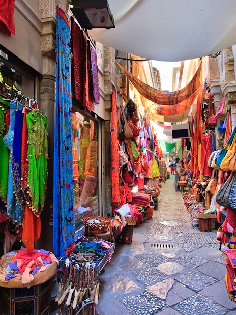 Colorful market street in Albaicin, Granada, with vibrant textiles and lanterns on display.