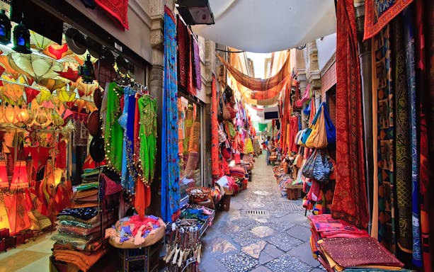 Colorful market street in Albaicin, Granada, with vibrant textiles and lanterns on display.