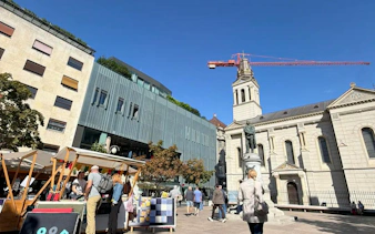 Outdoor market near historic church and modern buildings in Zagreb, part of self-guided city exploration game.