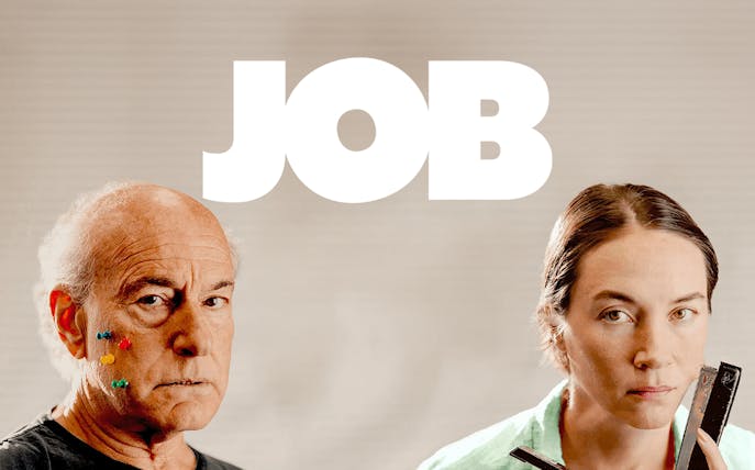 Two people with serious expressions, one with colorful pins on face, under the word 'JOB'.