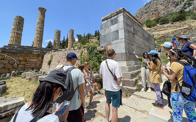 Tourists listening to guide at ancient ruins in Delphi, Greece during day trip.