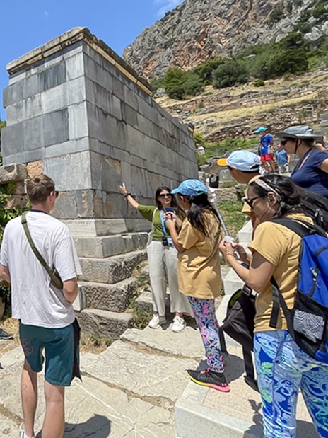 Tourists listening to guide at ancient ruins in Delphi, Greece during day trip.