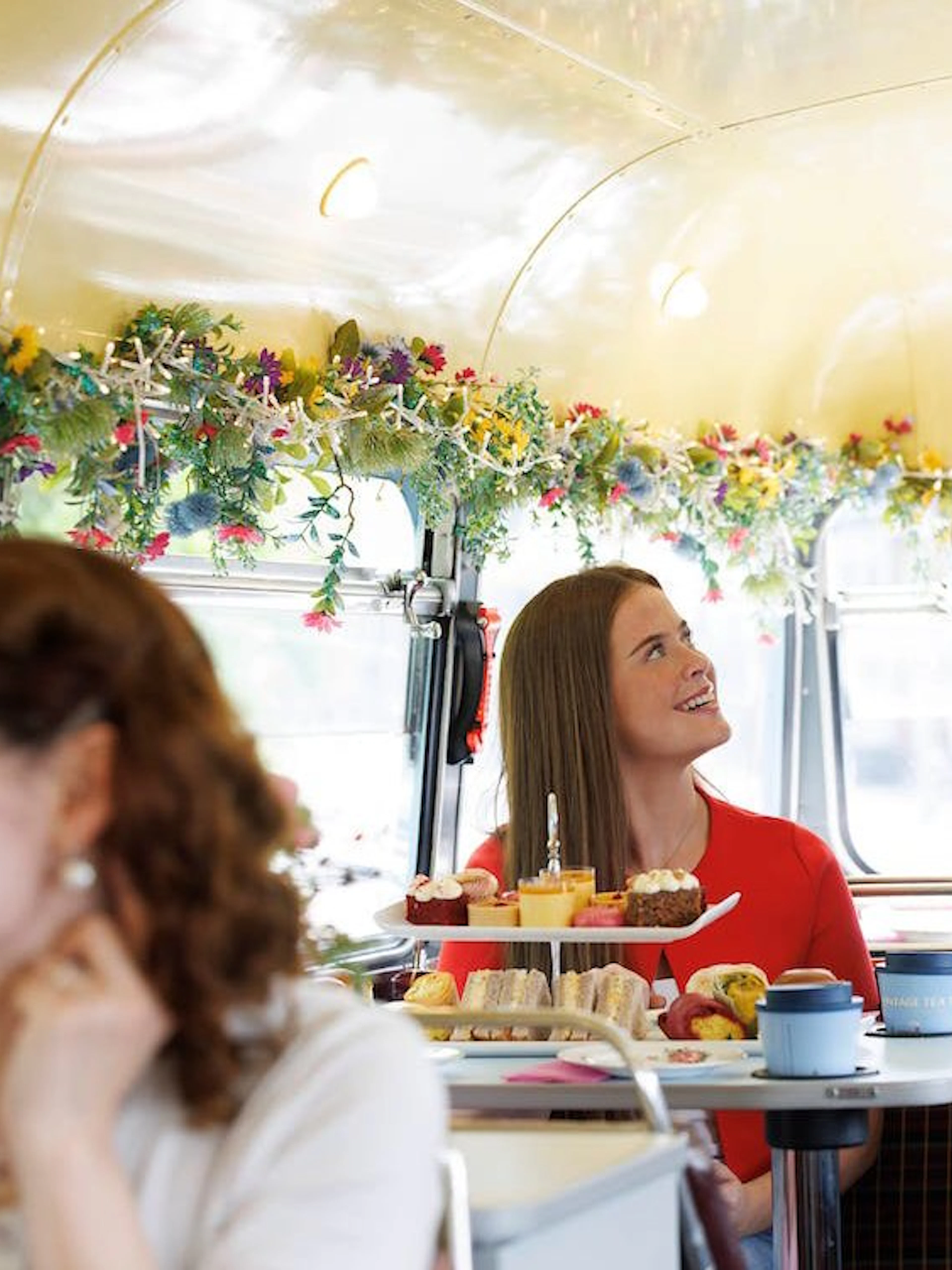 Server offering treats to guests on a vintage tea bus tour with floral decor.