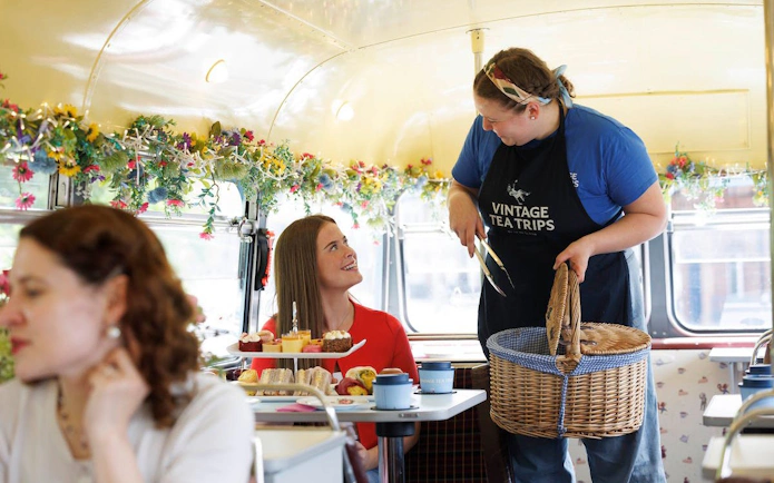 Server offering treats to guests on a vintage tea bus tour with floral decor.