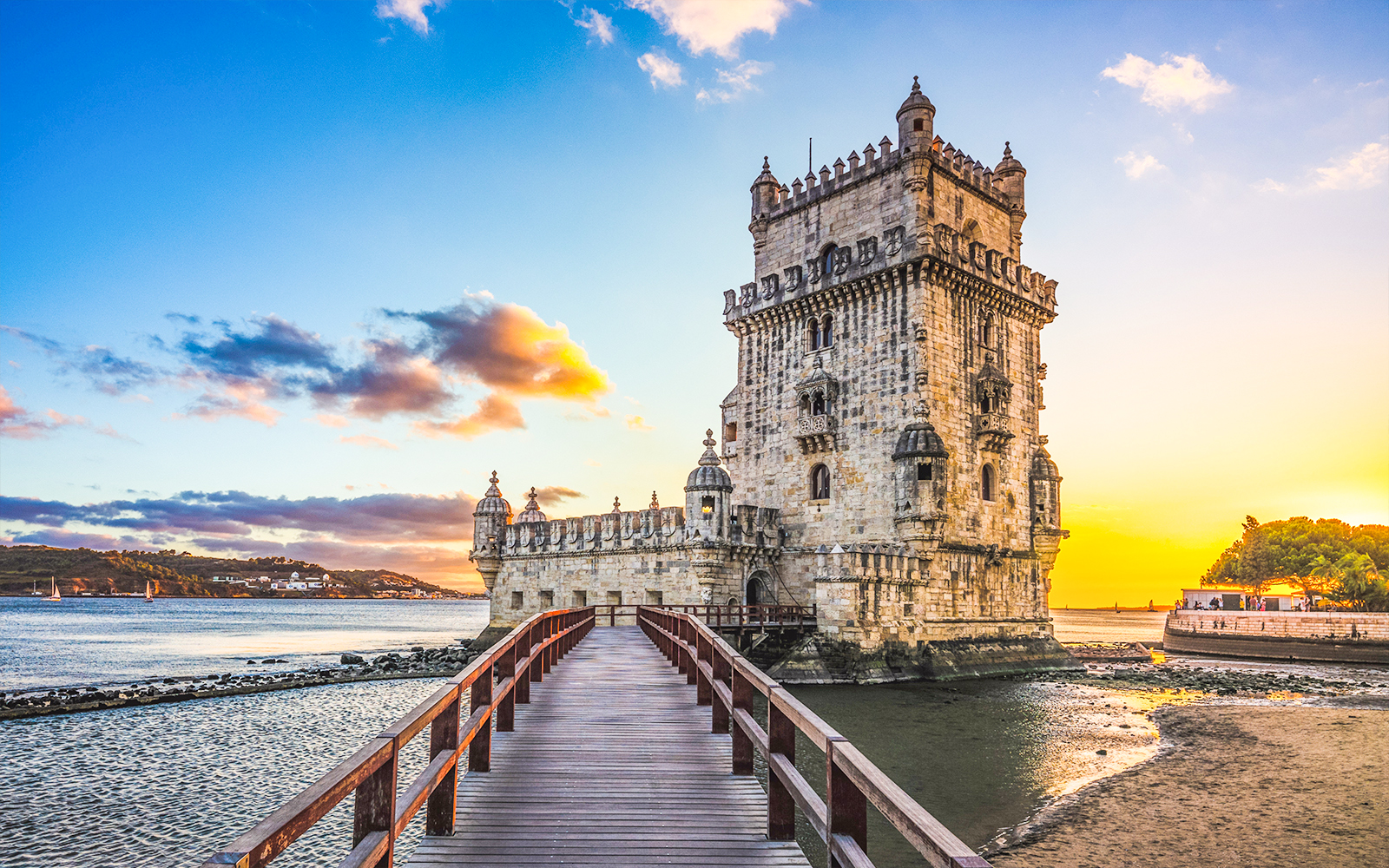 Belém Tower at sunset in Lisbon, Portugal, with a wooden walkway leading to the historic landmark.