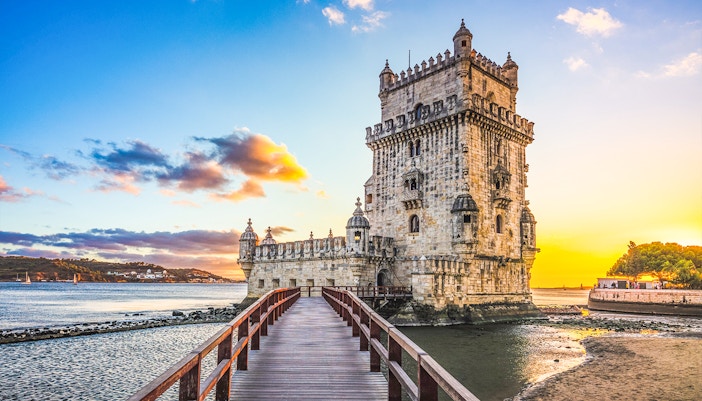 Belém Tower at sunset in Lisbon, Portugal, with a wooden walkway leading to the historic landmark.