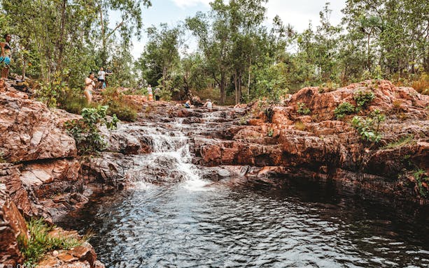 Waterfall cascading over rocky terrain in Litchfield National Park, Australia, with tourists exploring.