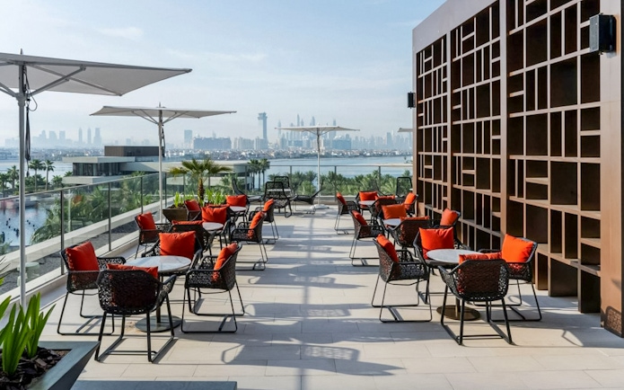 Rooftop dining area with red-cushioned chairs overlooking Dubai skyline at Gastronomy Buffet Dinner Experience.