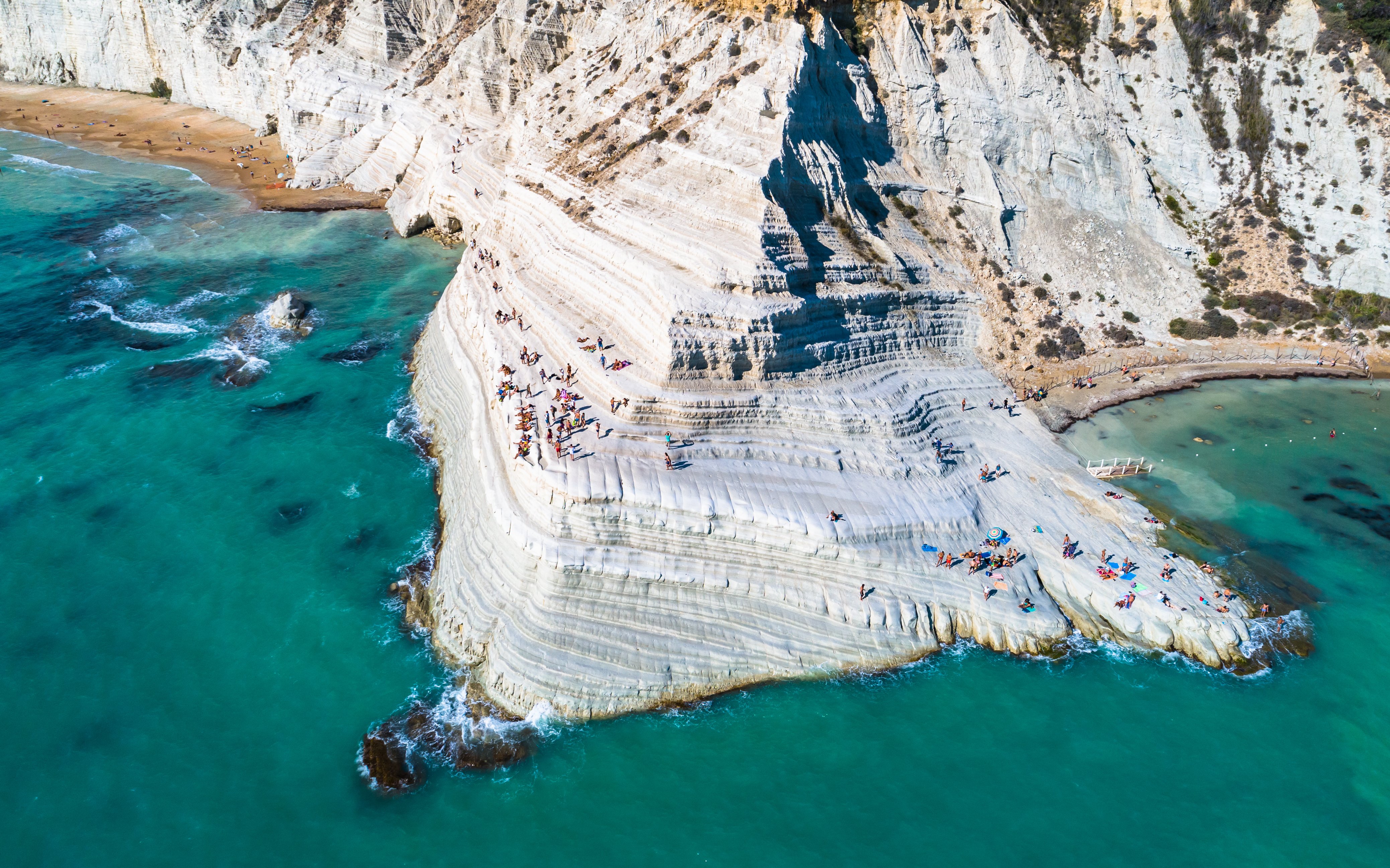Scala dei Turchi limestone cliffs with visitors sunbathing, Sicily coast.