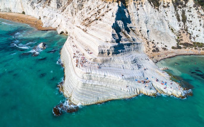 Scala dei Turchi limestone cliffs with visitors sunbathing, Sicily coast.