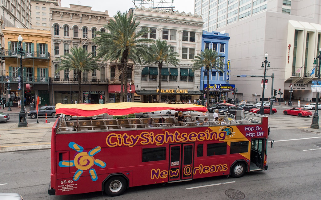 Open-top sightseeing bus on a New Orleans street with historic buildings in the background.
