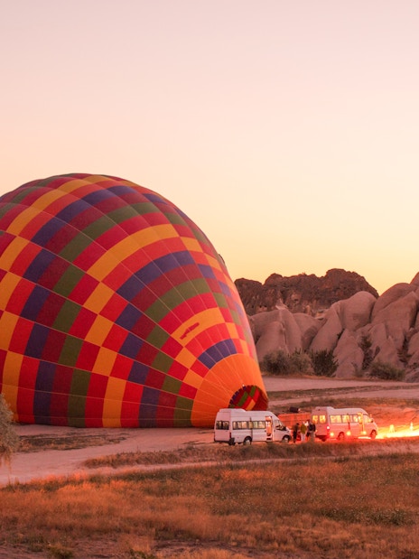 Hot air balloon inflating at sunrise in Cappadocia, Turkey with rocky landscape.