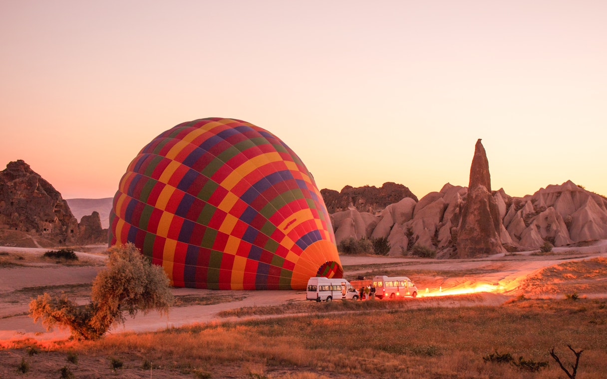Hot air balloon inflating at sunrise in Cappadocia, Turkey with rocky landscape.