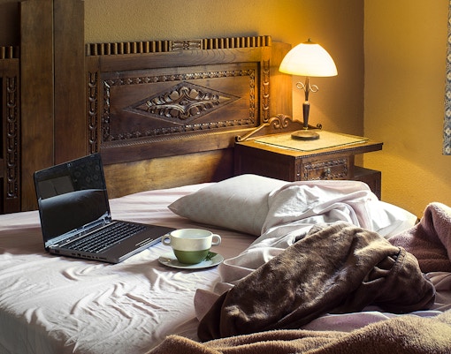 Rustic hotel room with wooden headboard, bedside lamp, and a laptop on the bed.