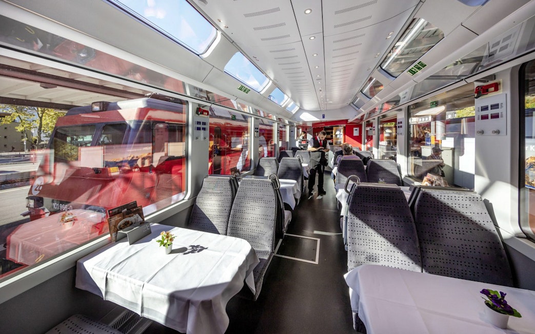 Interior of Lucerne–Interlaken Express train with dining tables and large windows.