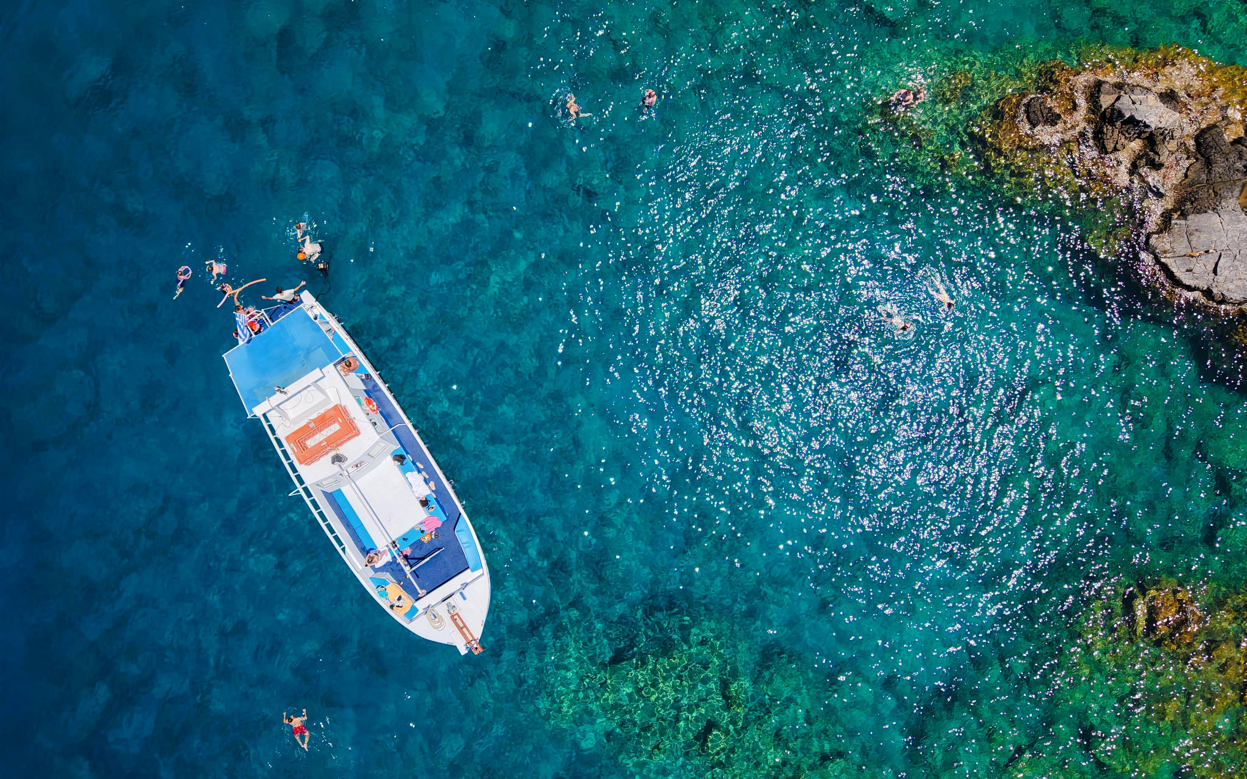 Boat with swimmers in turquoise sea during Lindos Sunset Cruise.