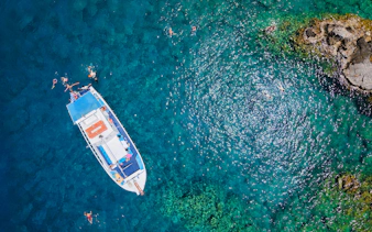 Boat with swimmers in turquoise sea during Lindos Sunset Cruise.