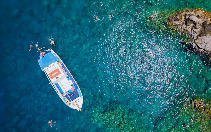 Boat with swimmers in turquoise sea during Lindos Sunset Cruise.