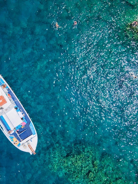 Boat with swimmers in turquoise sea during Lindos Sunset Cruise.